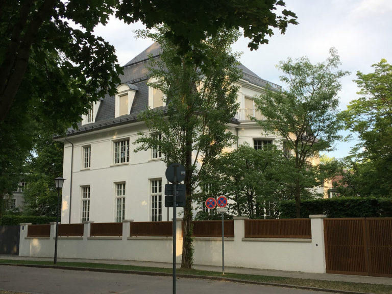 In der früheren Poschingerstraße stand das Haus, dass Thomas und Katia Mann sich 1913 bauen ließen und aus dem sie 1933 ins Exil gingen. In den 1950er Jahren wurden die Reste des beschädigten Gebäudes abgerissen. Der Nachfolgebau zitiert Elemente der Villa. An die Vorgeschichte erinnert ansonsten lediglich eine Gedenktafel an der weißen Mauer. Foto: Monika Gemmer